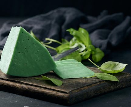 A piece of green cheese with basil on a brown wooden board, black background