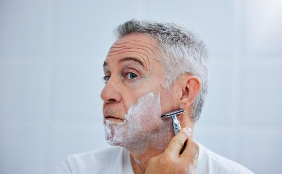 Its time for the beard to go. a mature man shaving his face in a bathroom at home.