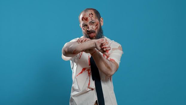 Ugly spooky mindless zombie giving thumbs down hand sign while standing on blue background.