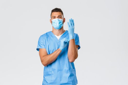 Healthcare workers, covid-19, coronavirus and preventing virus concept. Serious good-looking doctor, nurse in medical mask and scrubs, prepare for operation, surgeon put on rubber gloves