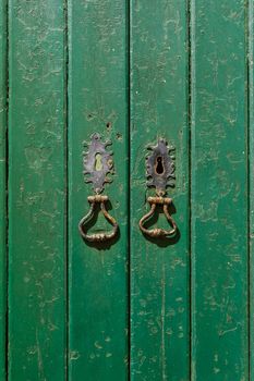 Antique door with peeling green paint, keyholes and metal rings