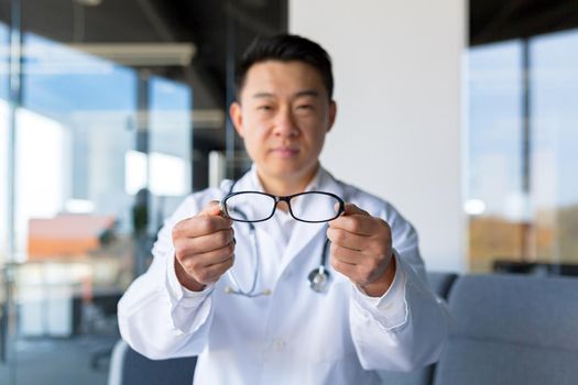 An Asian ophthalmologist offers glasses to a patient in a modern clinic