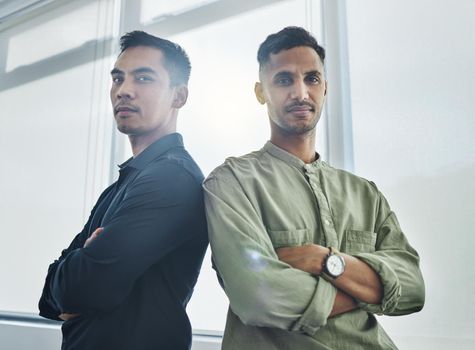 Weve got each others backs. Cropped portrait of two handsome young businessmen standing back to back with their arms folded in their office.