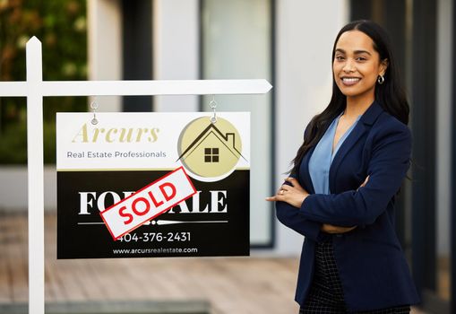 Another property sold. Cropped portrait of an attractive young real estate agent standing with her arms crossed in front of a sold sign outside of a recently sold home.