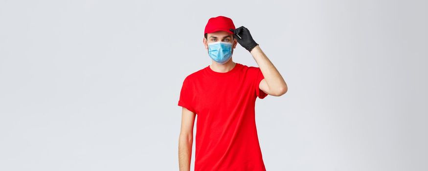 Covid-19, self-quarantine, online shopping and shipping concept. Friendly delivery guy saluting client as deliver groceries, packages to doorstem, self-quarantine orders, wear medical mask and gloves