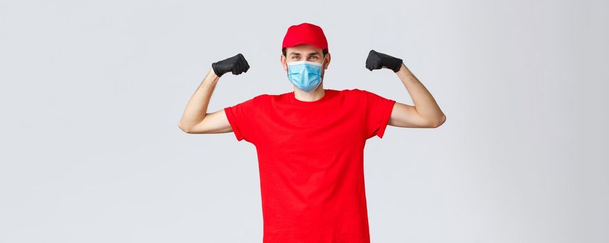 Covid-19, self-quarantine, online shopping concept. Strong delivery guy flexing biceps, showing strength, carry and transfer heavy large parcels to clients, express delivery to customer home