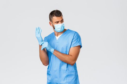 Healthcare workers, covid-19, coronavirus and preventing virus concept. Handsome male nurse or doctor, surgeon in blue scrubs and medical mask, put on gloves prepare to patient screening