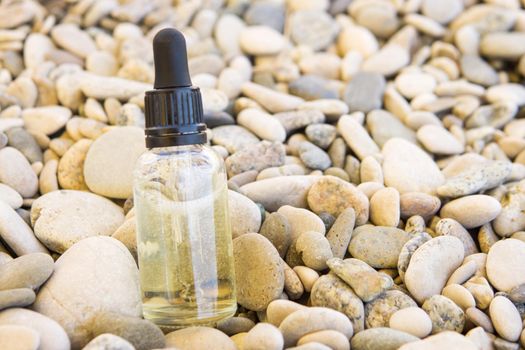 Cosmetic serum in a glass bottle with a pipette on stones