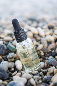 Cosmetic serum in a glass bottle with a pipette on stones