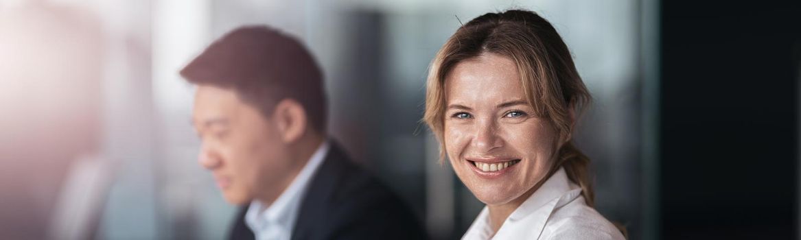 smiling businesswoman sitting at the office with colleague on background