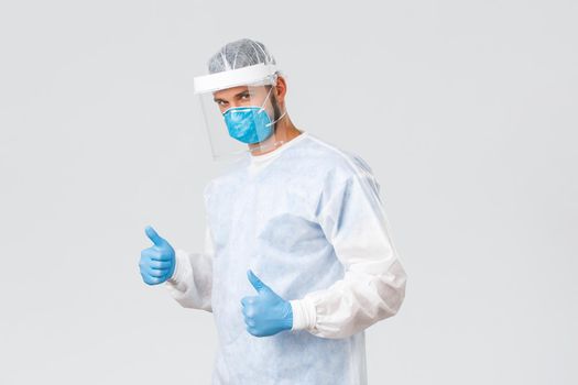 Covid-19 pandemic, virus outbreak, clinic and healthcare workers concept. Professional confident doctor in personal protective equipment, gloves and respirator, show thumbs-up, no problem