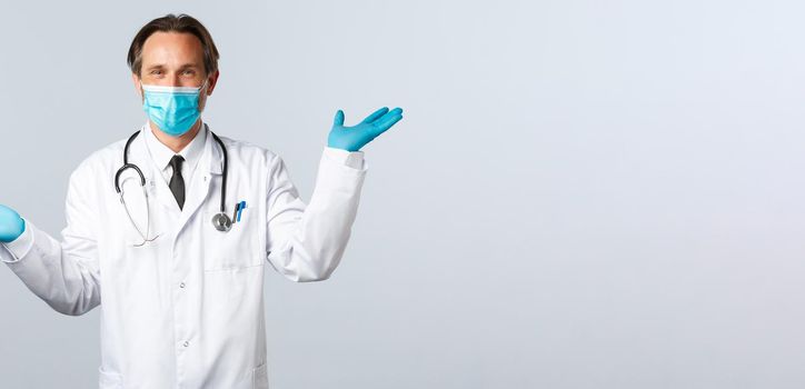 Covid-19, preventing virus, healthcare workers and vaccination concept. Smiling handsome doctor give two variants, wear medical mask and gloves, showing left and right products, white background