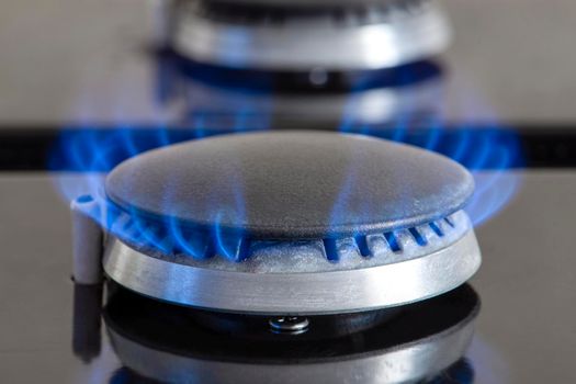Combustion of natural gas, propane. Gas stove on a black background. Fragment of a gas kitchen stove with a blue flame, close-up. Energy crisis concept, rise in price or price of gas.