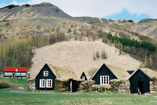Black wooden houses with moss-covered roofs in a mountain valley. Iceland