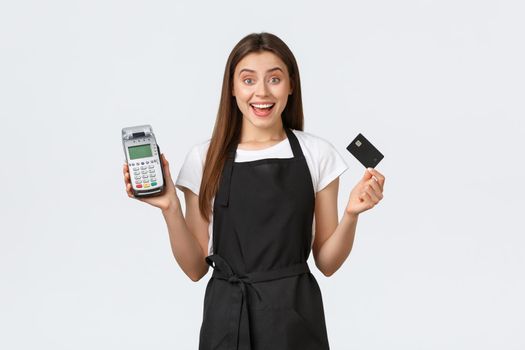 Grocery store employees, business and coffee shops concept. Excited smiling cafe worker, cashier in black apron showing how easy and safe purchase items contactless with credit card and POS terminal