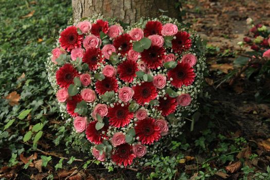 Heart shaped sympathy flowers  or funeral flowers near a tree, pink roses and gerbers and Eucalyptus