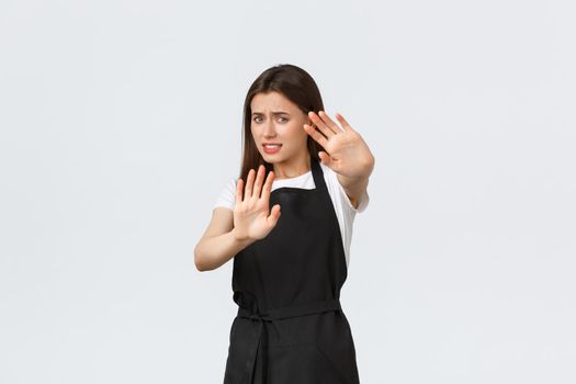 Grocery store employees, small business and coffee shops concept. Displeased young female cafe worker protect herself from flashlight or cameras of strange visitor, white background