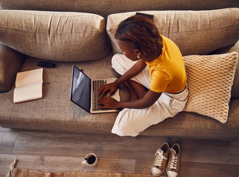Distance learning student writing, studying and typing on a laptop doing a virtual assignment test on the sofa at home. Above view of one young female writer or language editor typing an essay online