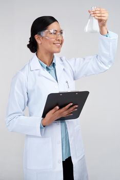 Examining the sample. an attractive young female scientist examining a beaker filled with liquid in studio against a grey background.
