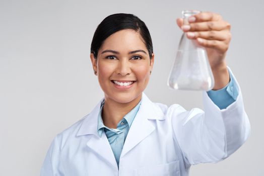 A scientist cant help but conduct research. Cropped portrait of an attractive young female scientist holding a beaker filled with liquid in studio against a grey background.