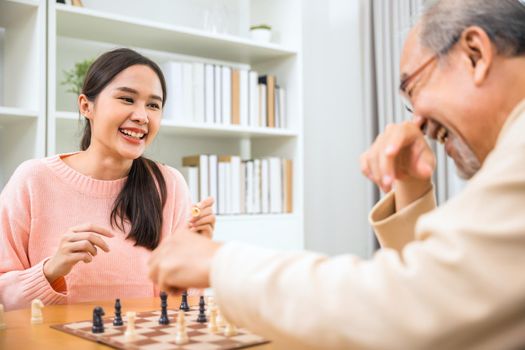 Beautiful young smile woman having fun sitting playing chess game with senior elderly at home