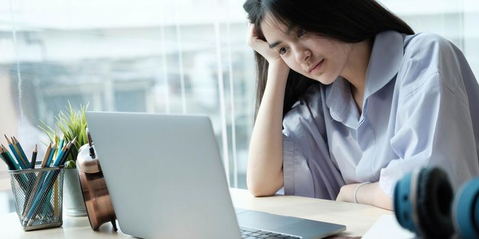 Asian girls are sitting stressed studying online with a tutor on a laptop while sitting in the bedroom at home night. Concept online learning at home
