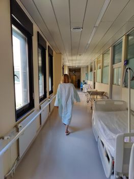 Female patient wearing hospital robe walking in long empty hospital hallway.
