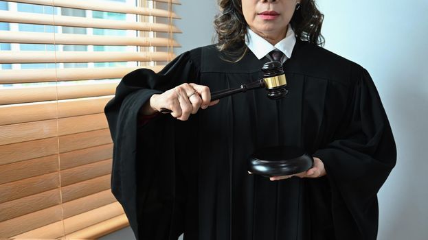 Mature female judge, lawyer or attorney dressed in robe gown uniform with gavel hammer mallet. Law and justice concept