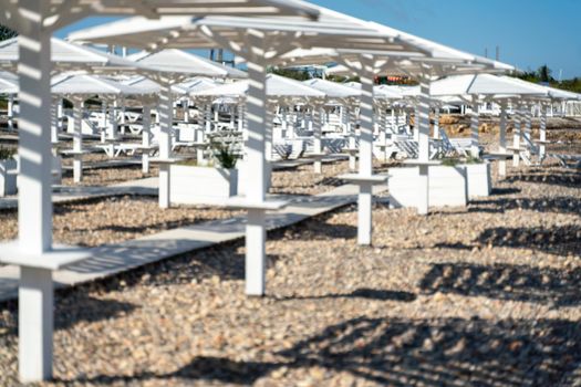 Rows of wooden umbrellas from the sun on the seashore in the morning. Wooden paths on the sand between umbrellas. Beach holiday at the resort.