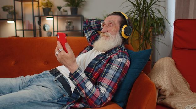 Happy relaxed man in wireless headphones dancing listening favorite rock n roll music on home couch