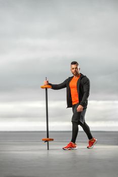 Bodybuilder athlete in orange sportswear doing barbell exercises in the outdoors gym. Powerful fitness workout.