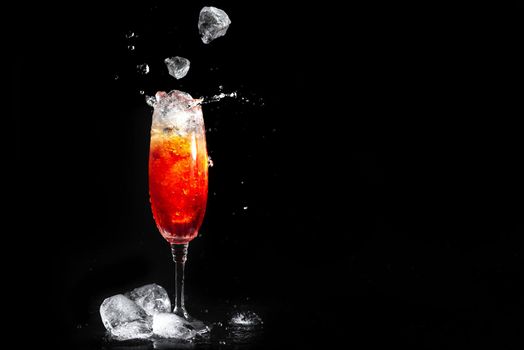 Glass with Aperol Cocktail on black background. Ice falls into the glass with the alcoholic beverage. A splash of cocktail aperol. Summer drink.