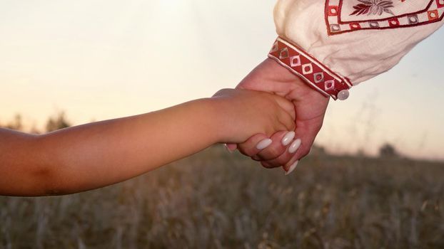 Mom and child holding hands together on wheat field sunset background. Son takes mother hand. Family, trust, love and happiness concept