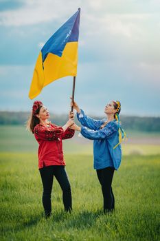 Happy ukrainian women raised national flag, it flies as symbol of love for Motherland. Friends in embroidery vyshyvanka - national blouses. Ukraine, independence, patriot symbol