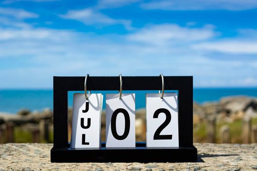 Jul 02 calendar date text on wooden frame with blurred background of ocean.
