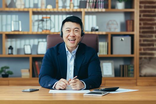 Happy Asian businessman boss looks at the camera smiling and talking to a colleague