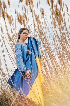 Sorrowful ukrainian woman with national flag on natural reeds background. Lady in blue embroidery vyshyvanka blouse. Ukraine, independence, freedom, patriot symbol, victory in war.