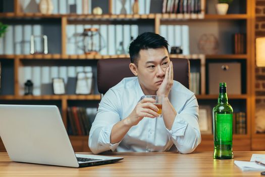 Asian businessman fails, man in despair drinks hard liquor, sitting late at the table