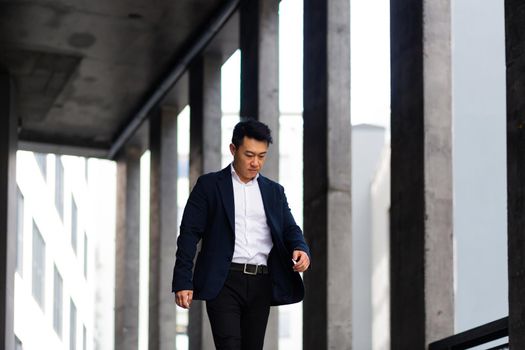 Asian businessman goes for a walk near a modern office center in a hurry