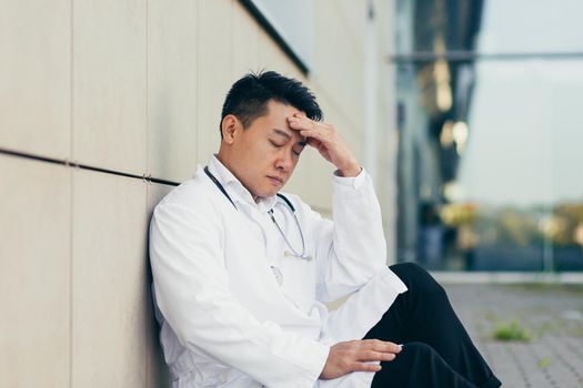 portrait Doctor Asian man tired after work sitting on the floor near the clinic disappointed