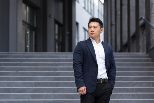 Portrait of asian serious businessman near office in business suit confident broker sales manager