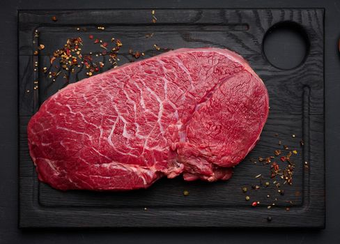 Raw beef tenderloin lies on a brown wooden board, black table. 