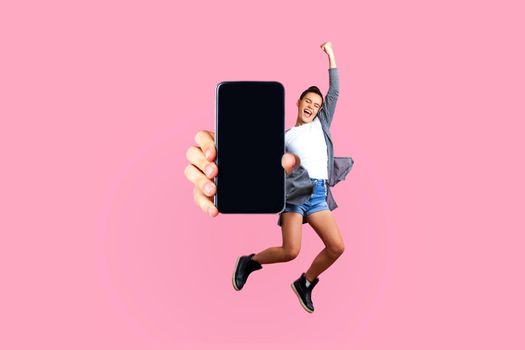 Happy teenager girl flying and jumping in air and showing big mobile empty screen