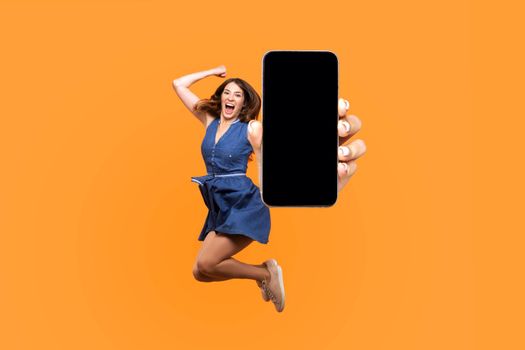 Happy young woman flying and jumping in air and showing big mobile empty screen