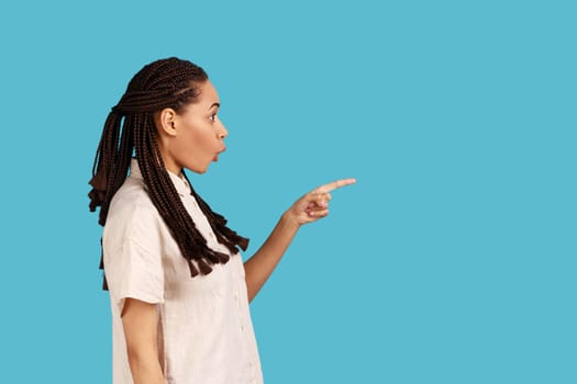 Surprised woman with dreadlocks points away with finger, showing blank space for your advertisement.