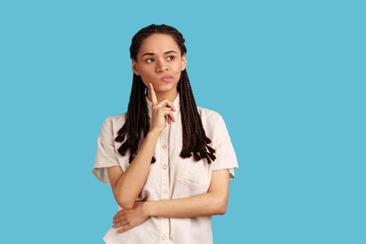 Woman with black dreadlocks thinking about future, holding chin, having serious facial expression.
