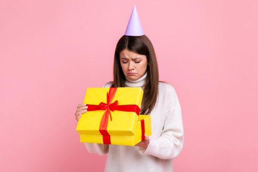 Disappointed female in party cone looking inside wrapped present box, open gift, unpleasant surprise