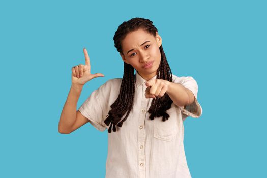 Serious woman with dreadlocks showing loser gesture and pointing at camera, accusing for failure.