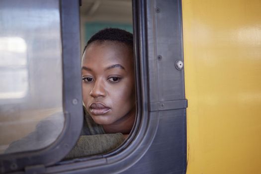 Leaving the past behind. a young woman looking depressed while staring out the window of a train.
