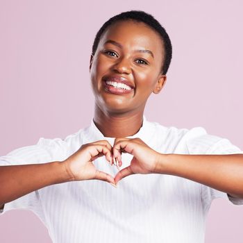 Sending you so much love. Portrait of a young woman making a heart gesture with her hands against a pink background.